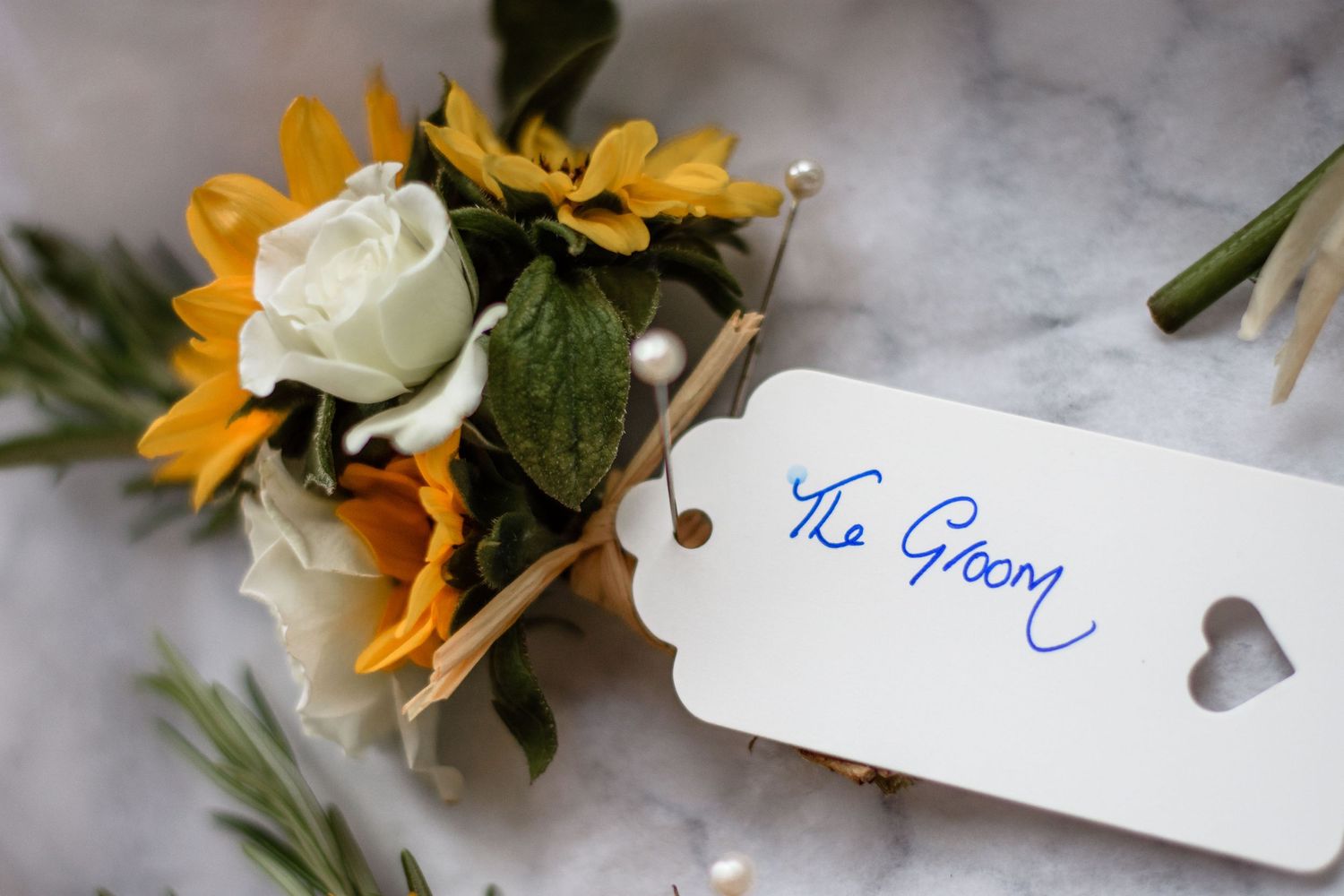 Wedding flower arrangement with sunflowers and white roses next to a groom's name tag.