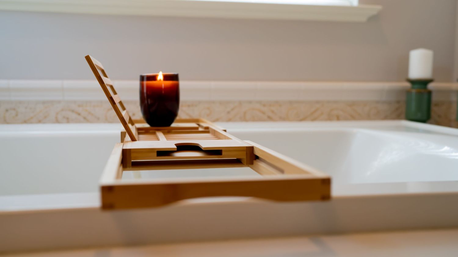 Wooden bath caddy with red wine glass resting on white bathtub edge.