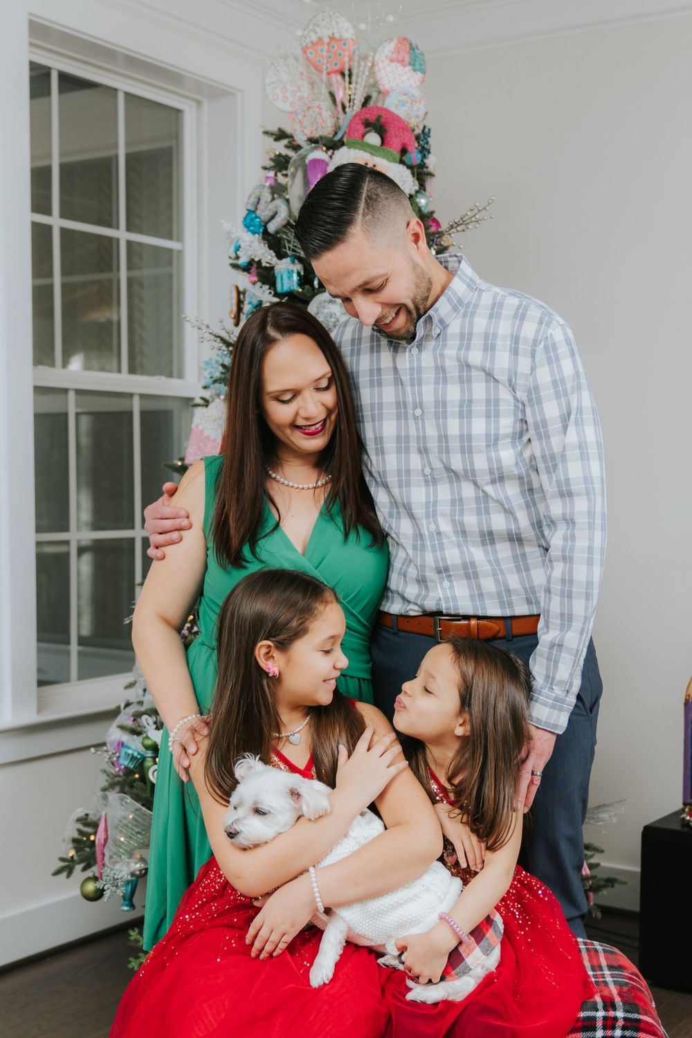 Family poses together by decorated Christmas tree with white pet rabbit.