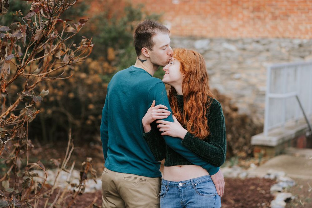 Romantic couple embraces outdoors against brick wall backdrop during autumn season.
