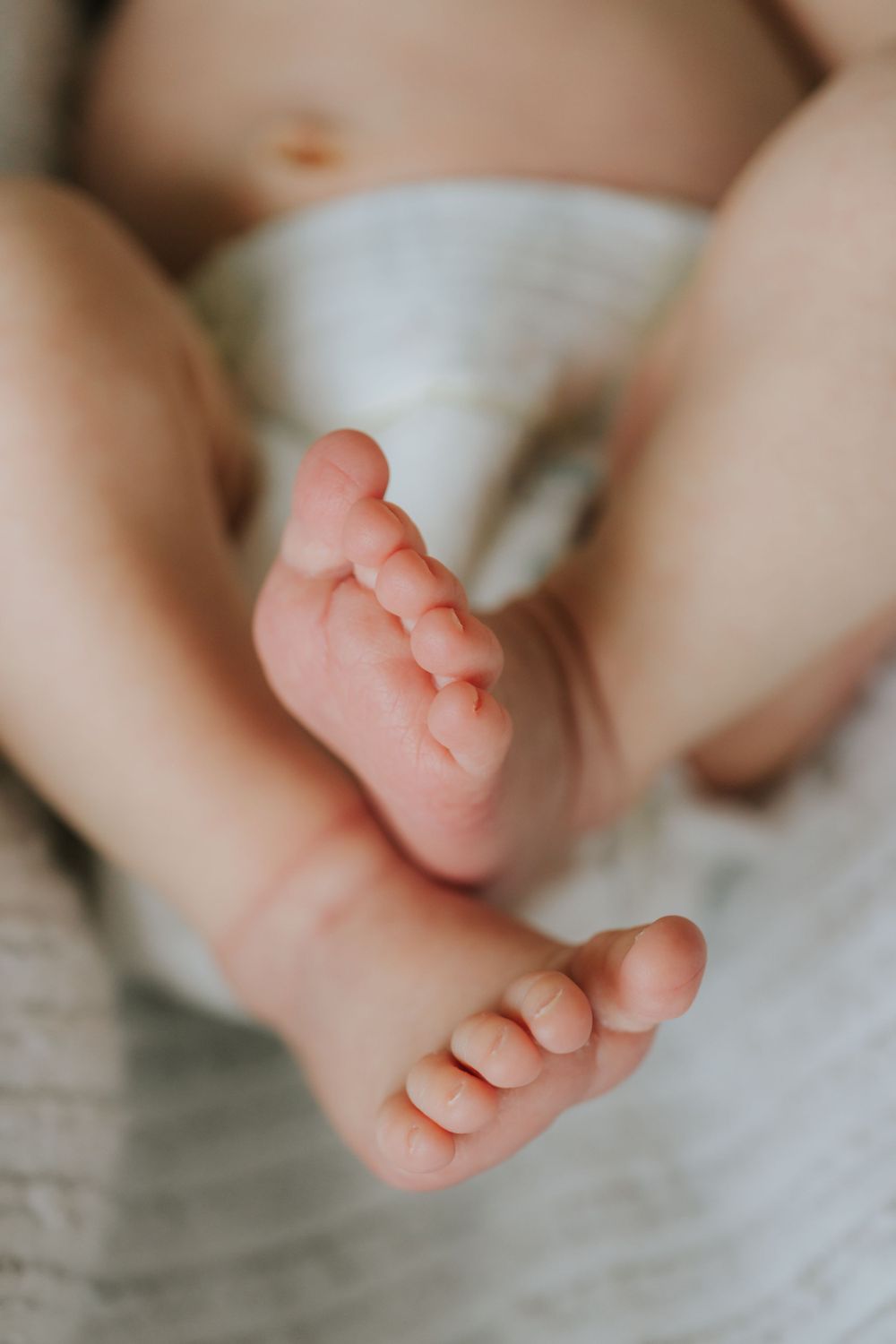 Close up of tiny baby feet resting on white bedding.