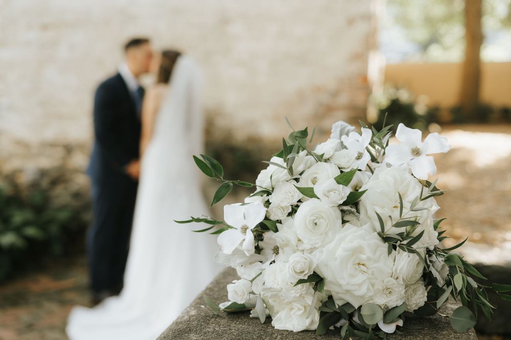 White floral bouquet in foreground with couple blurred in background.