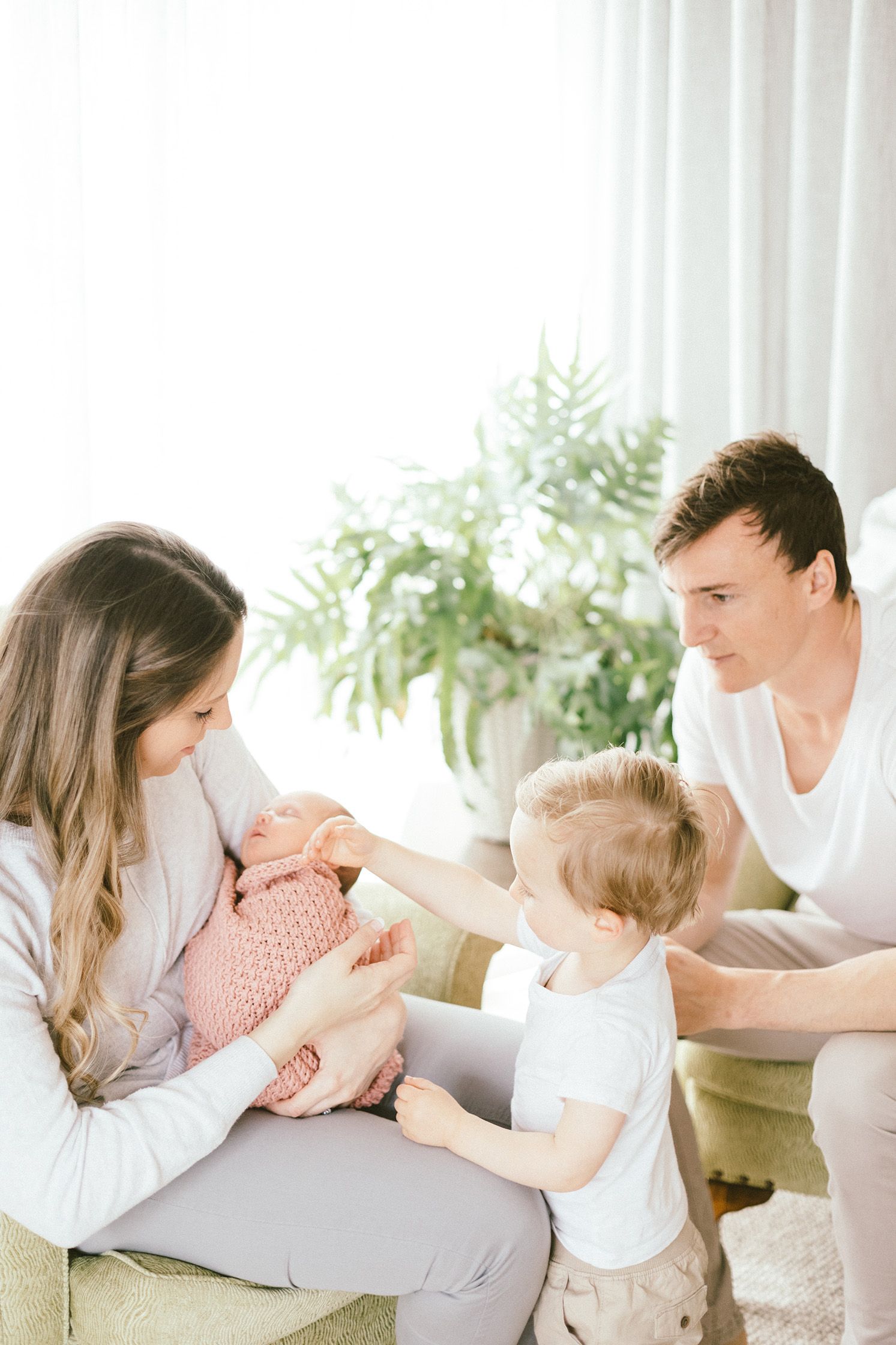 Parents sharing sweet playful moments with their newborn on a cozy sofa.