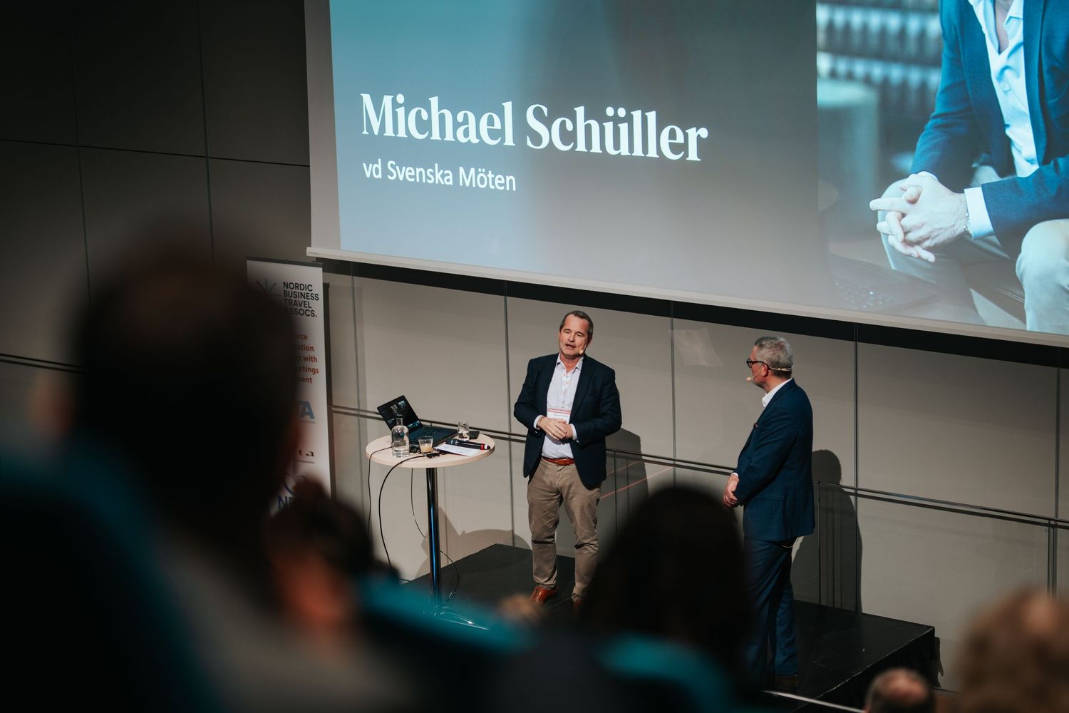 Business presentation featuring Michael Schüller speaking on stage at a corporate event.