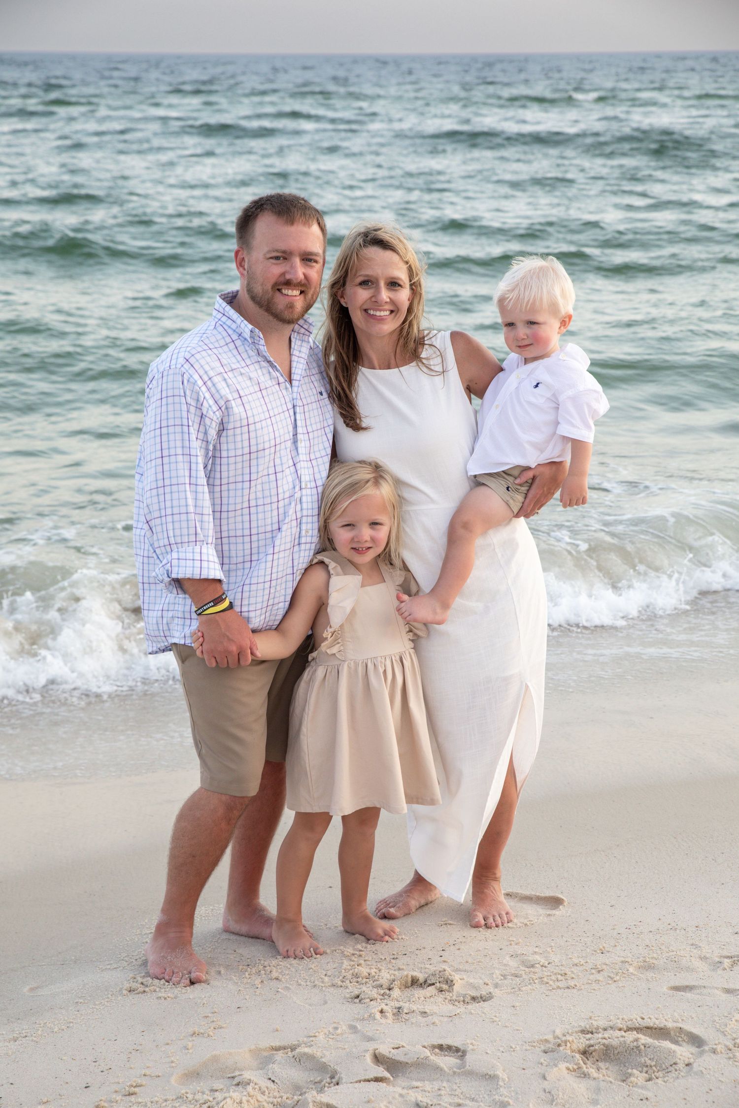 Family portrait on a sandy beach with turquoise ocean waves in the background.