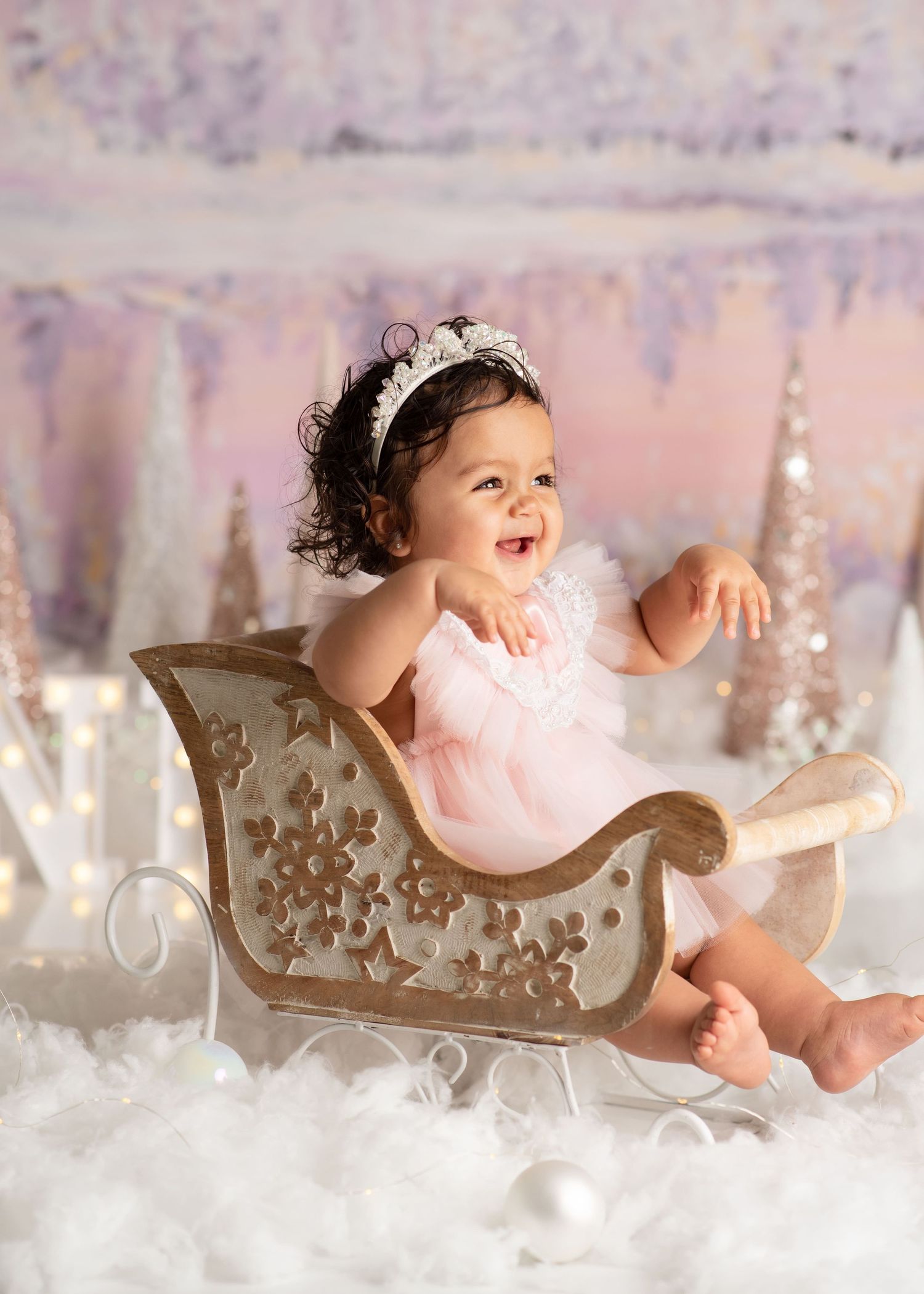 from her winter onederland, a baby smiles brightly with her arms raised while sitting in a tiny sleigh