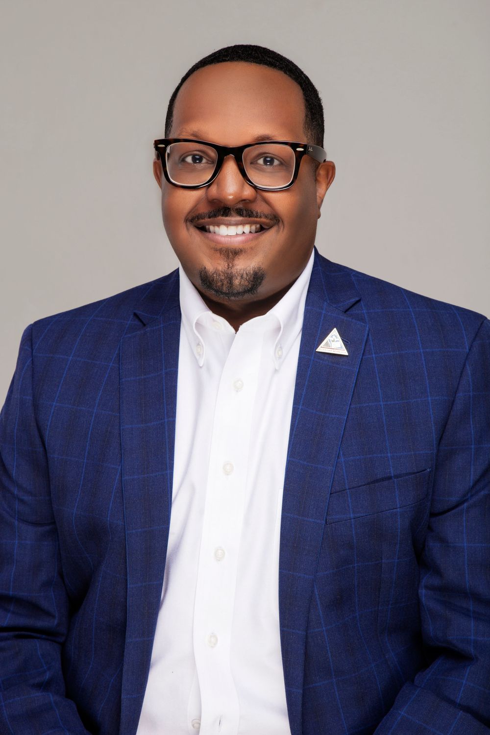Professional headshots of a person in a blue checkered blazer and white shirt against grey background.
