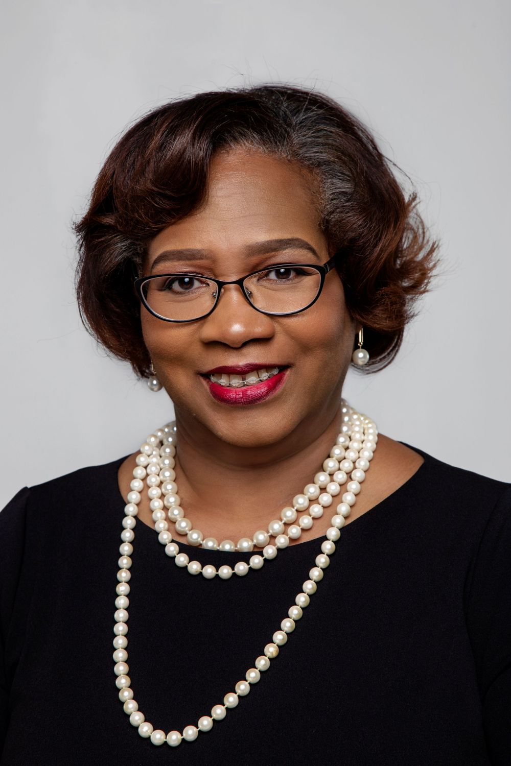 Portrait series showing a person in black attire with pearl necklace and glasses against grey background.