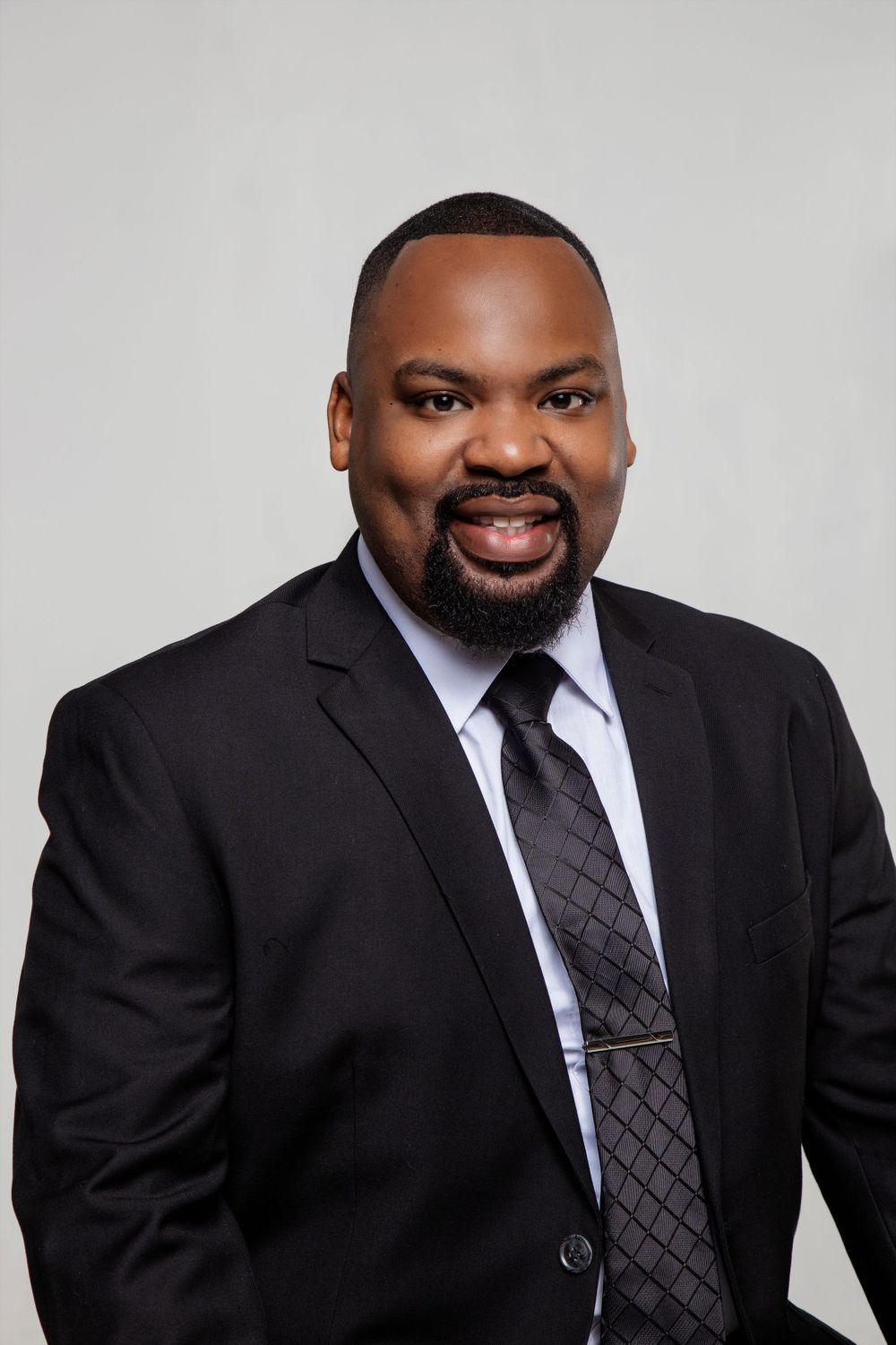 Professional headshots of a person in dark suit and tie smiling against grey background.
