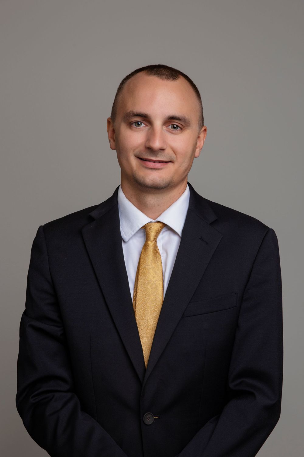 Business portrait series of a person in black suit with yellow tie against neutral backdrop.