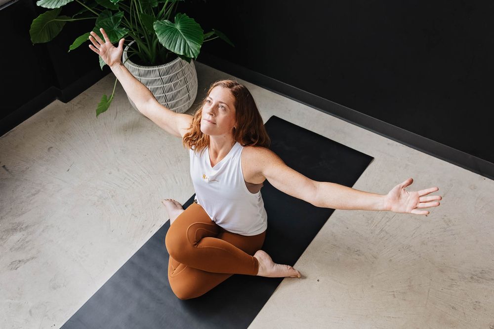 Person in athletic wear performing yoga poses on a black mat next to a decorative plant.
