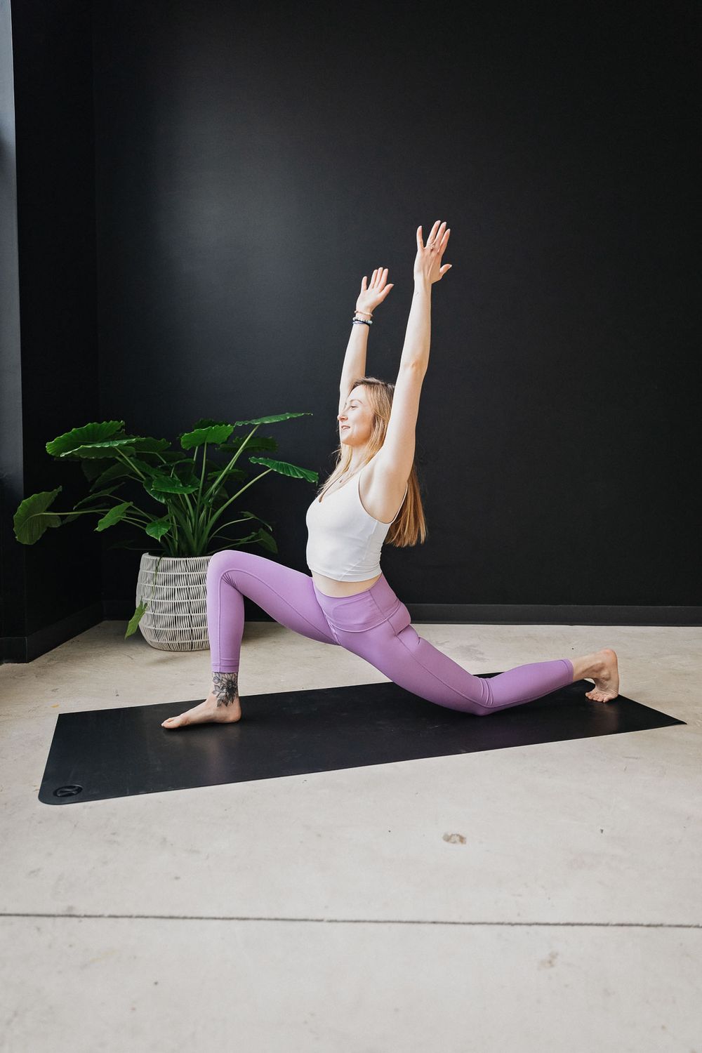 Yoga practitioner performing a series of stretching poses on a black mat against dark wall with potted plant.