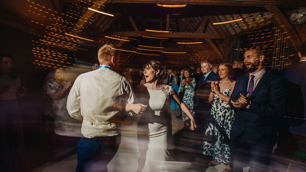 People dancing and celebrating on a dimly lit wedding reception dance floor.