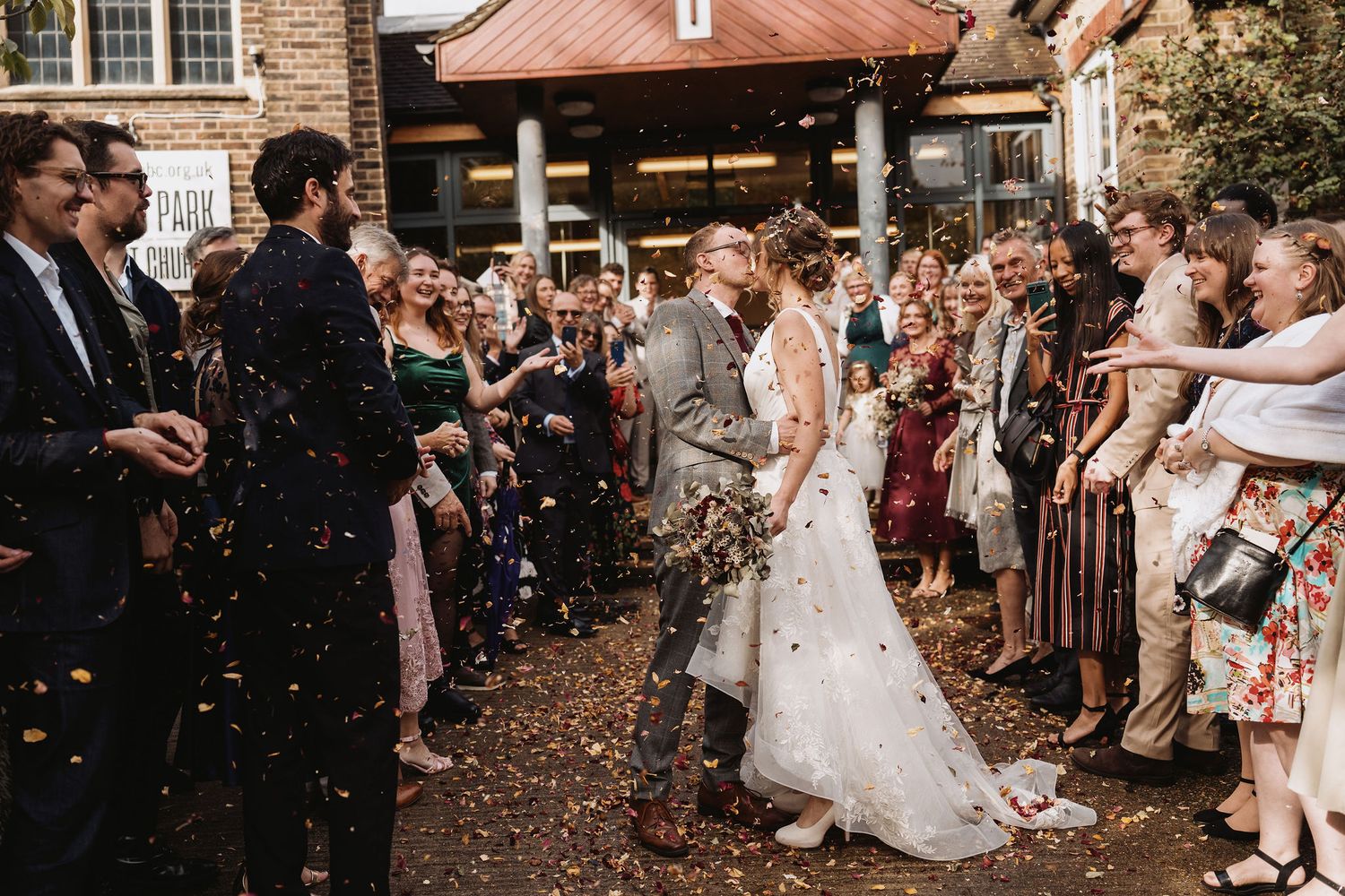 Wedding guests throw confetti as newlyweds exit through a crowd in an outdoor ceremony.