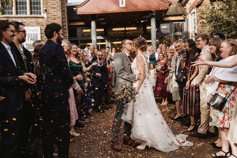 Wedding guests throw confetti as newlyweds exit through a crowd in an outdoor ceremony.