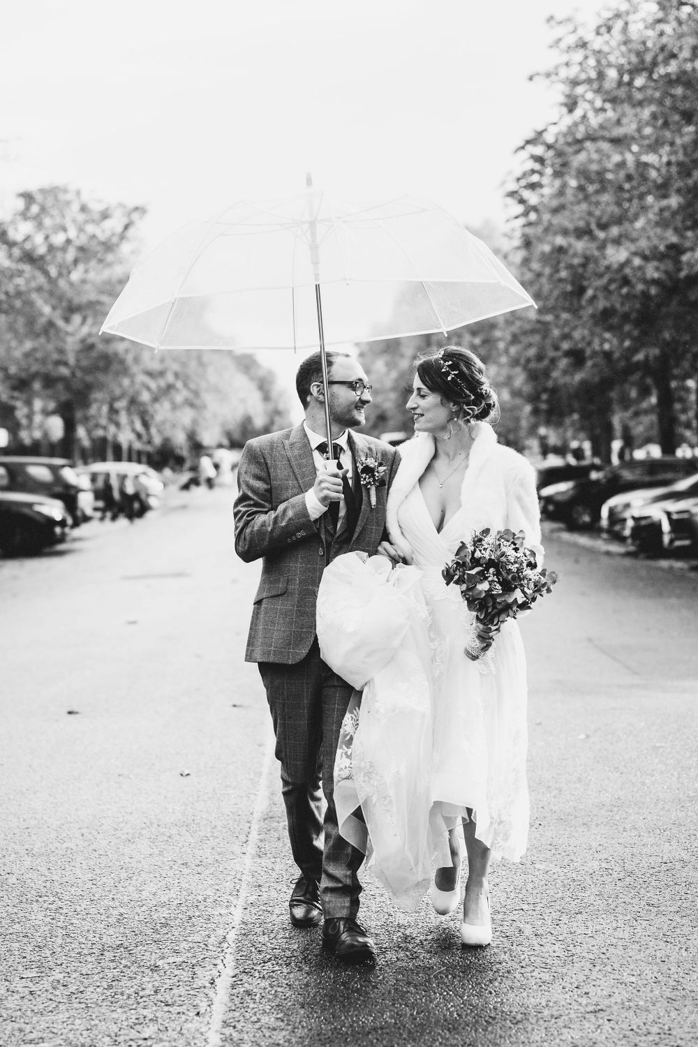 A couple shares an umbrella while walking in the rain on their wedding day.
