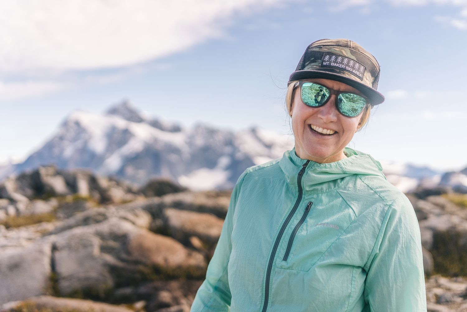 Hiker in turquoise jacket enjoys mountain views on a sunny day.
