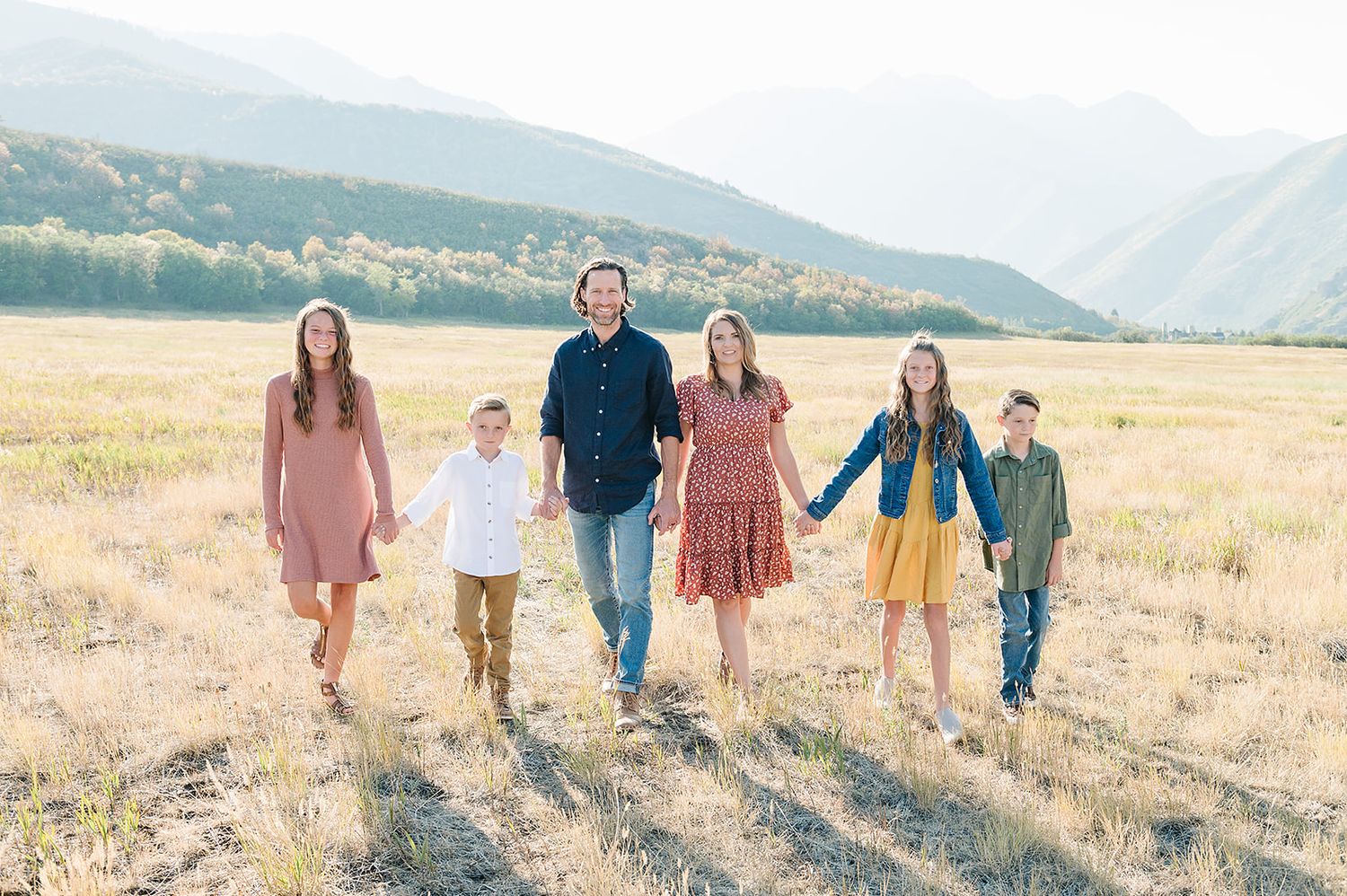 A family walks together through a golden mountain meadow at sunset with mountains in the distance.