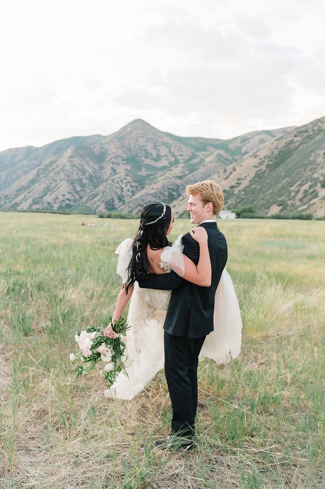 Newlyweds share an intimate moment in a mountain field with dramatic peaks in background.