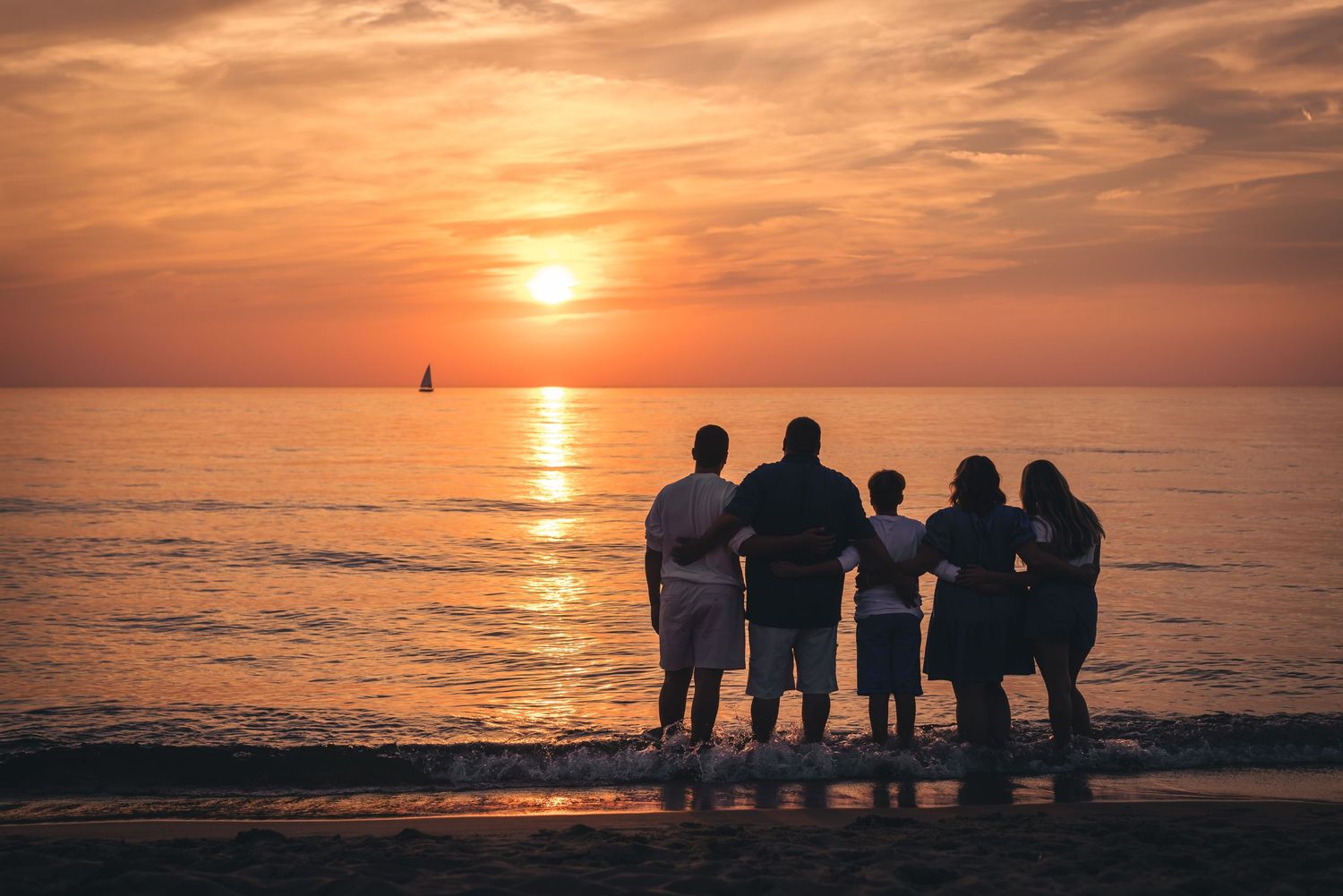 Silhouettes of a group watching the sunset over a calm ocean horizon.