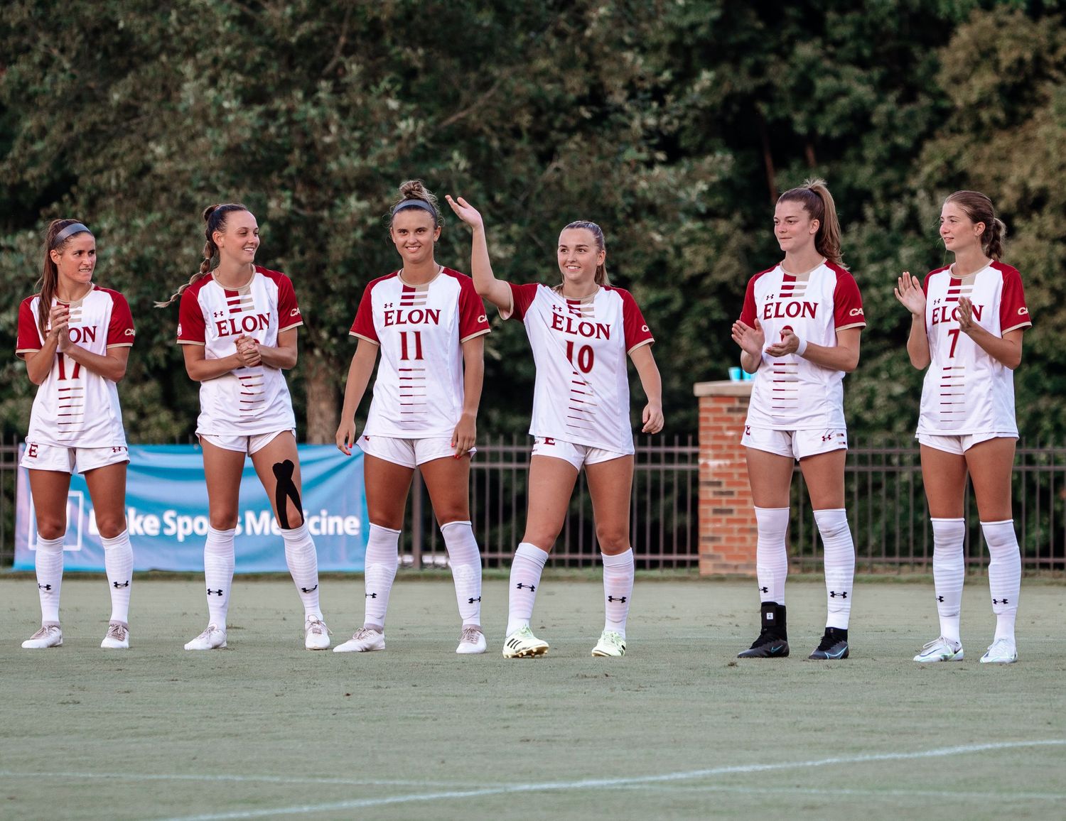 Group of athletes in white uniforms pose together on a sports field for a team photo.