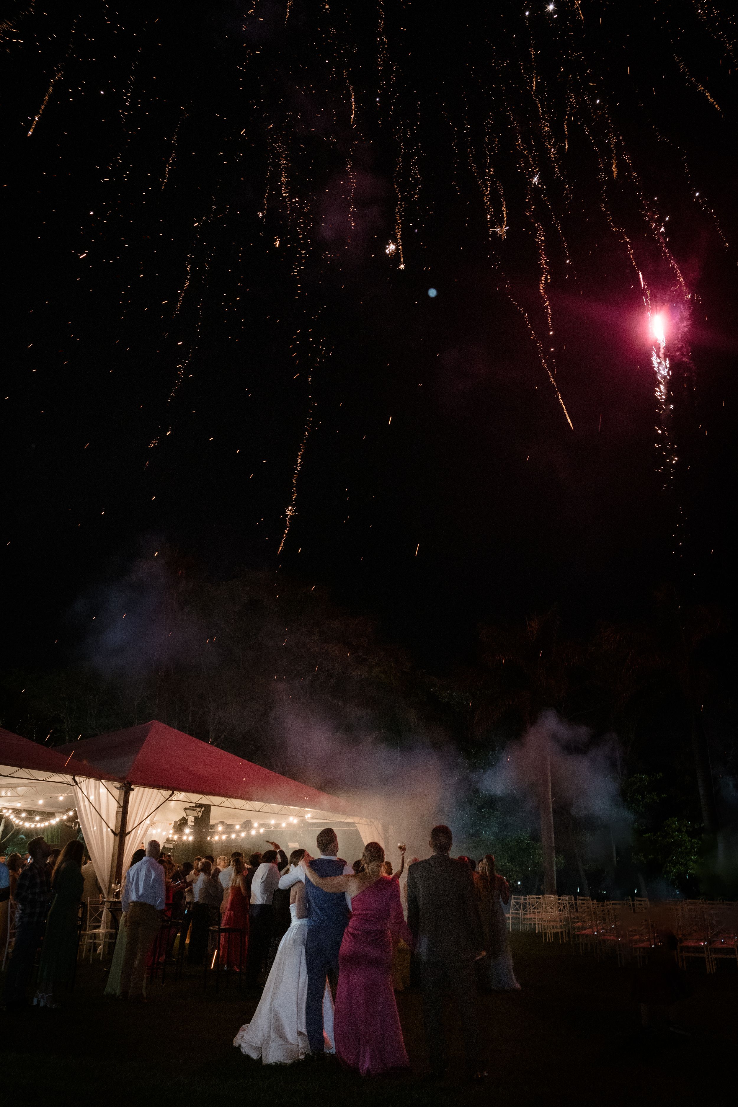 Fireworks display lighting up the night sky over outdoor wedding tent celebration.