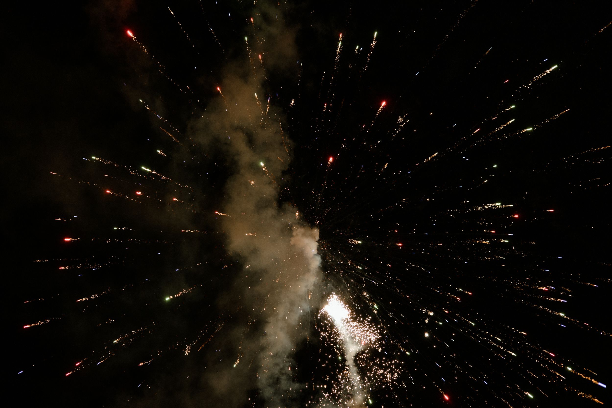 Colorful fireworks bursting in night sky with smoke trails.