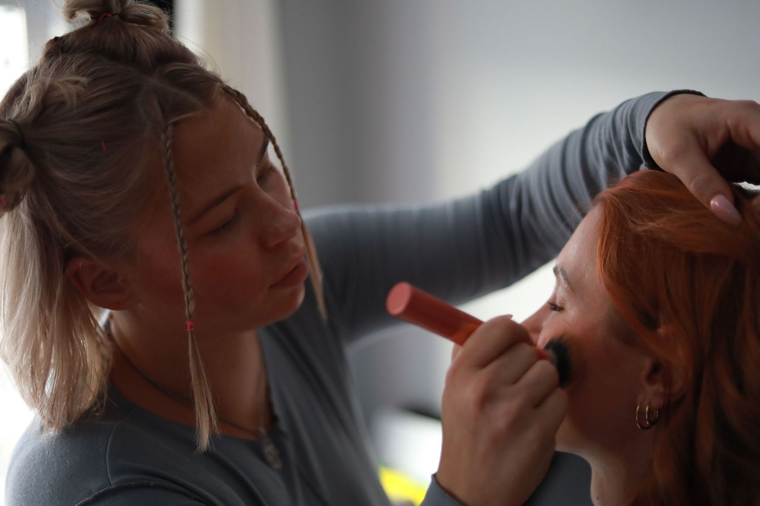 Makeup artist applying cosmetics to a client in natural lighting.