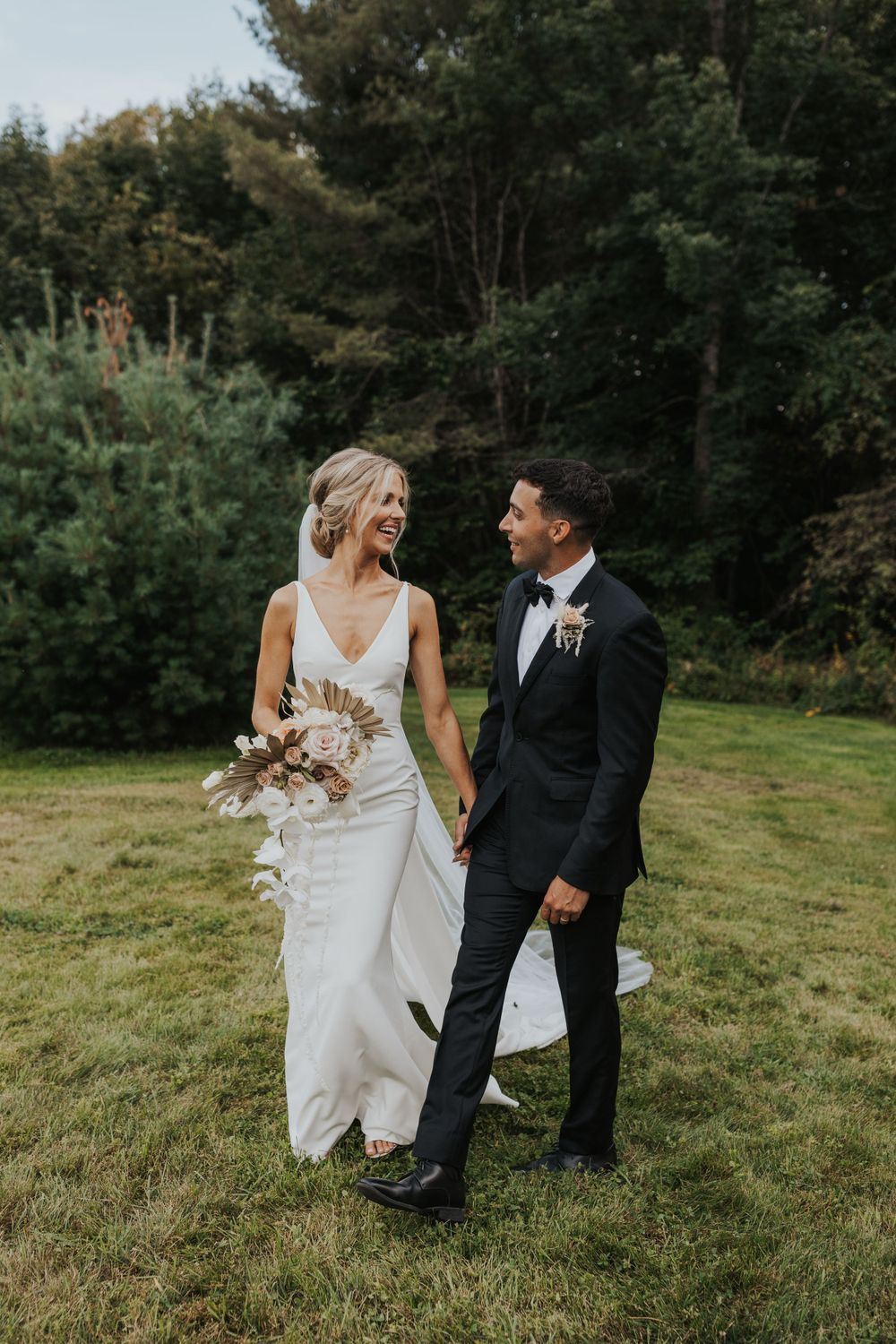 Couple shares a candid moment on grassy field during outdoor wedding photoshoot.