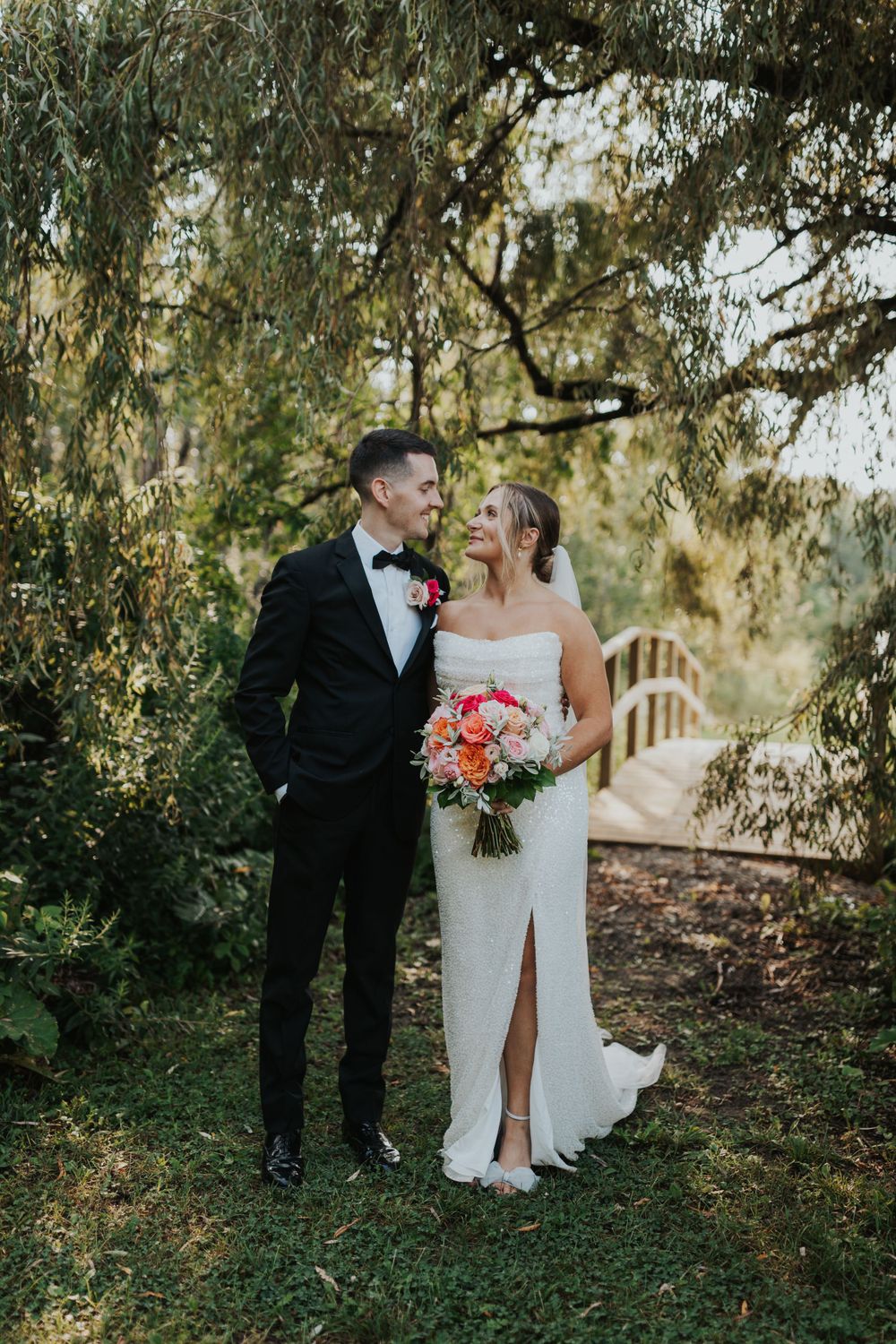 A joyful bride and groom share a laugh in an outdoor garden setting with natural lighting and vibrant greenery.
