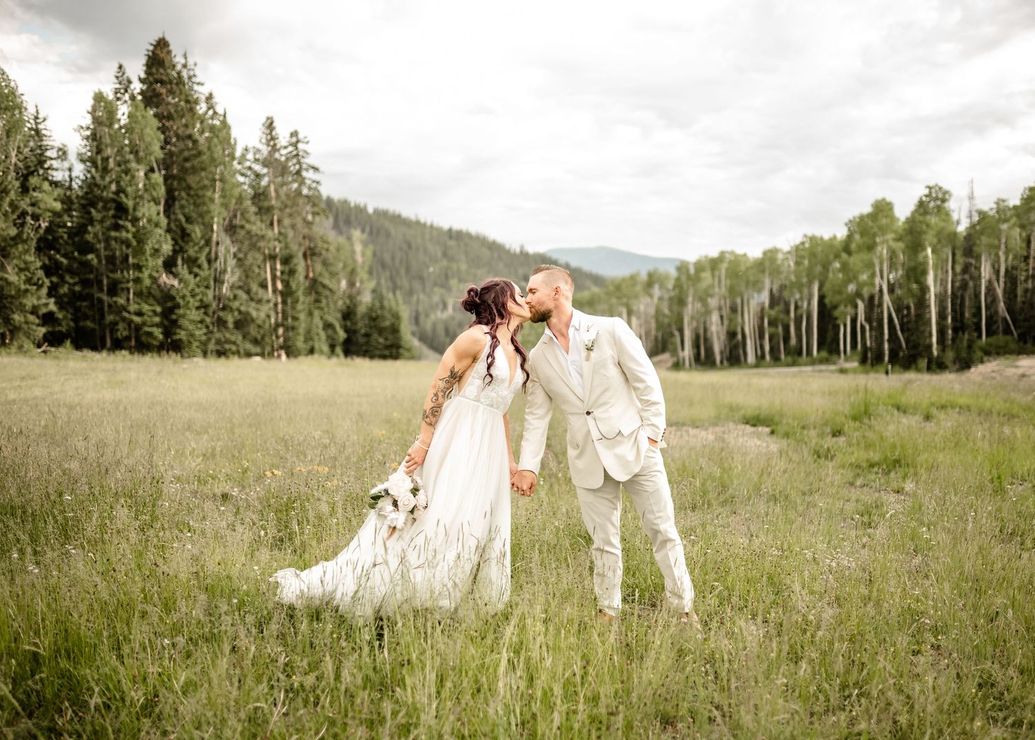 A couple walks hand in hand through a scenic mountain meadow filled with wildflowers.