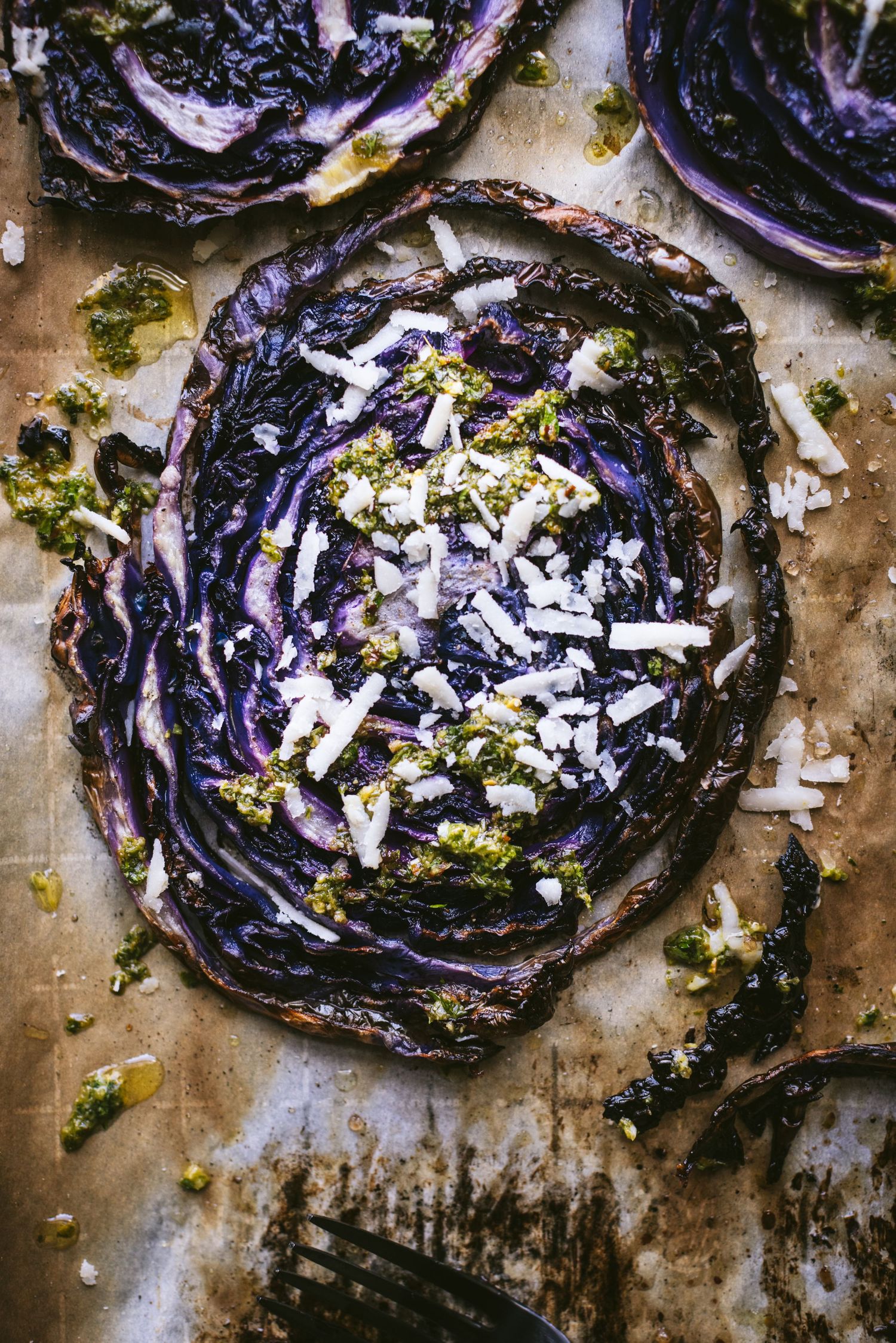 Charred purple cabbage steak topped with green pesto and shredded Parmesan cheese on parchment.