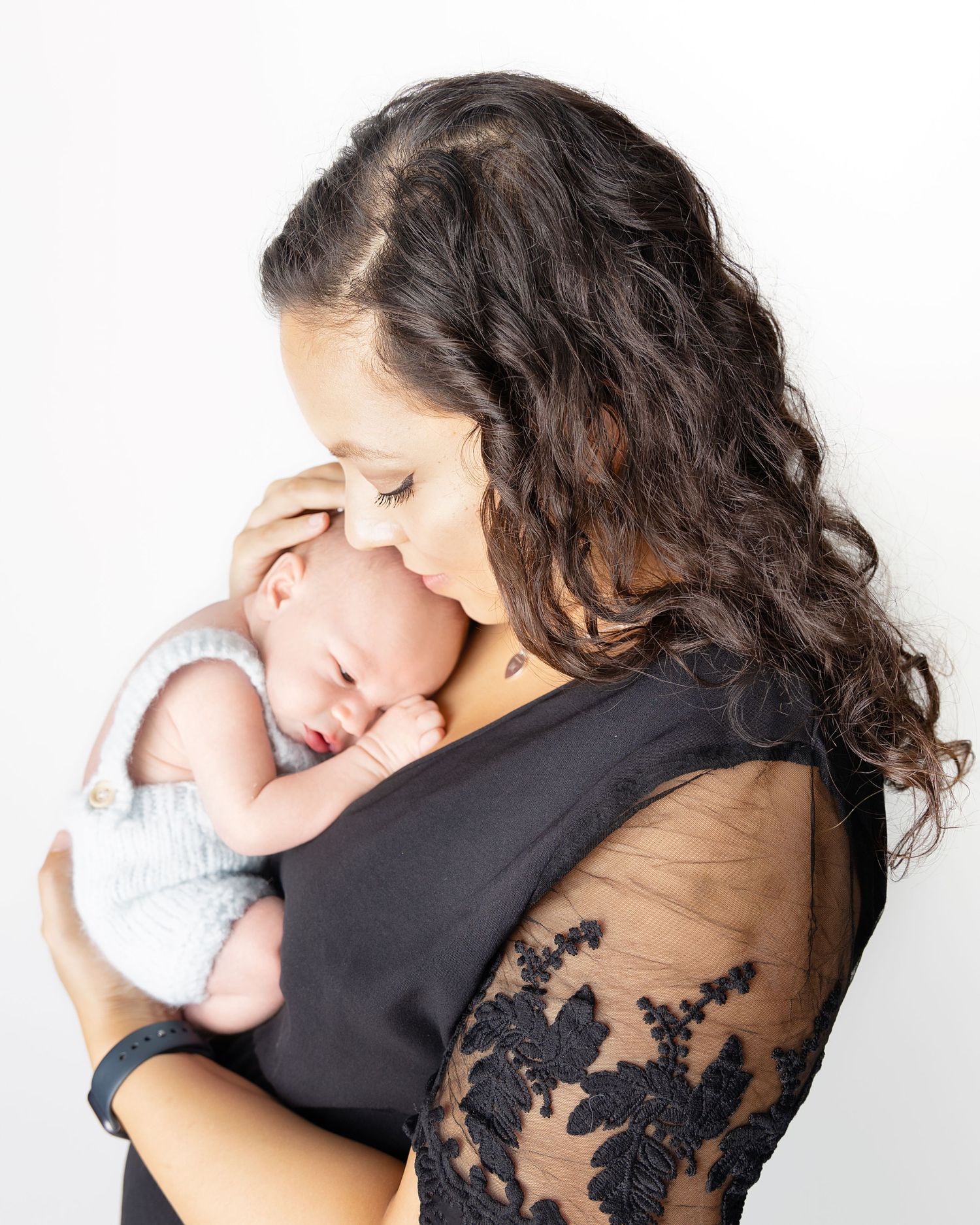 A tender moment between a mum in black lace dress and a sleeping newborn baby cradled against her chest.