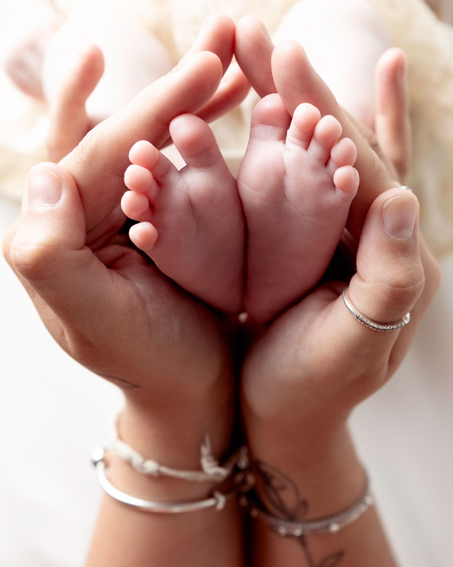 Small infant feet cradled gently in adult hands wearing delicate silver bracelets.