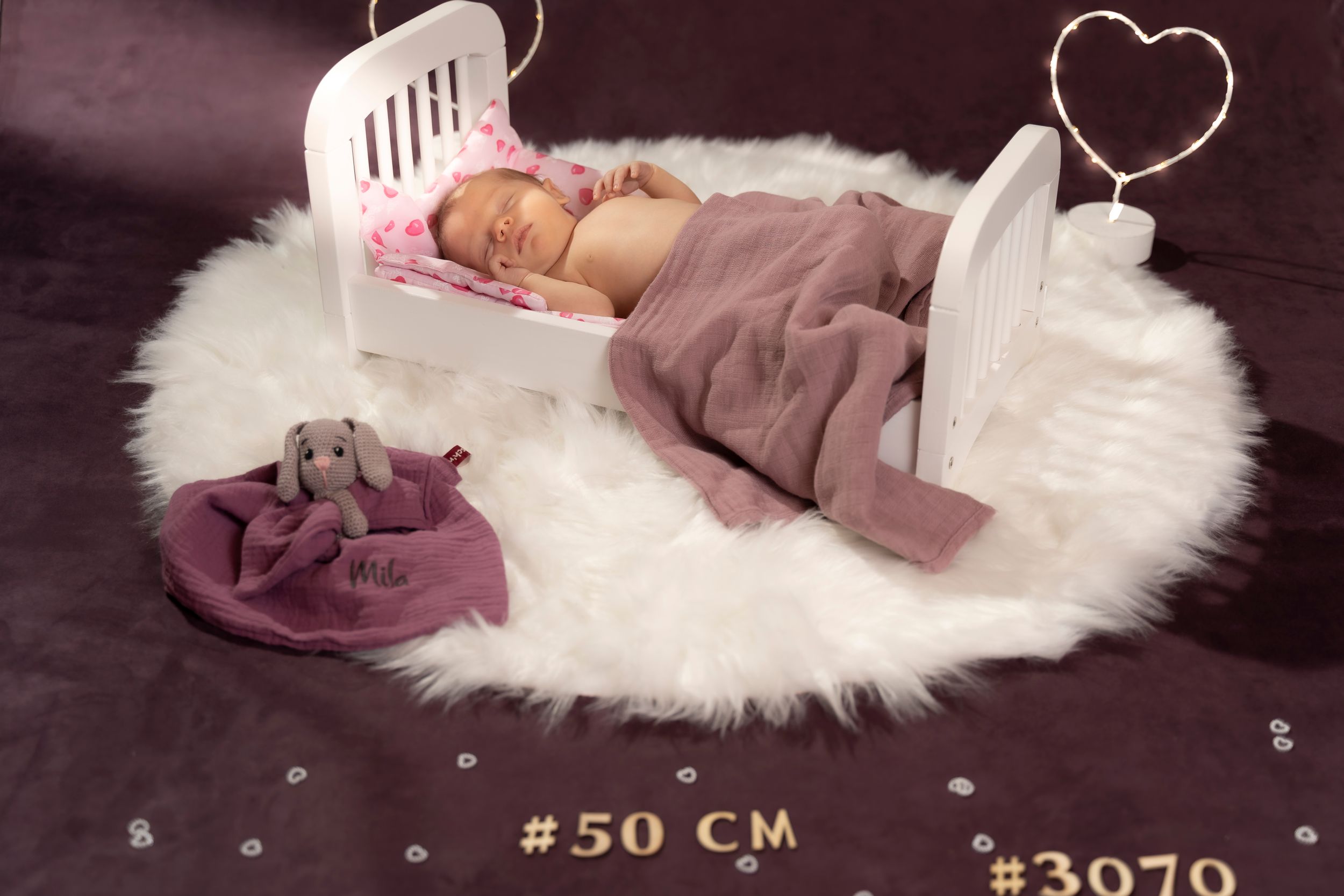 Newborn baby sleeping on white fur rug with heart decoration.