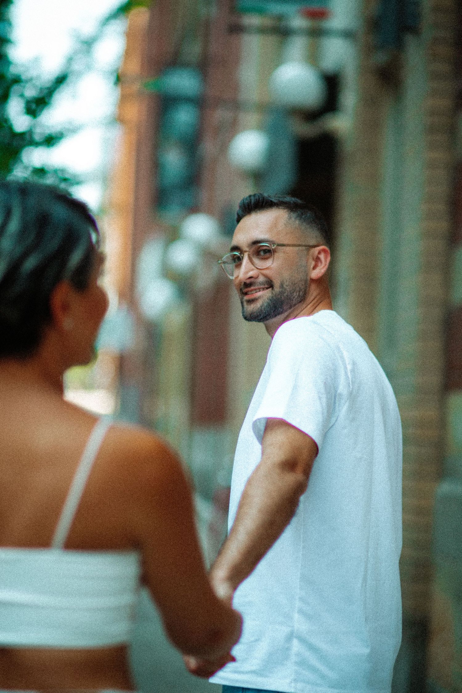 A casual urban photoshoot of a couple in white tops against a brick building backdrop.