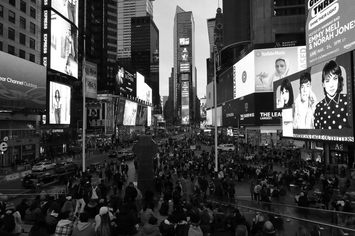 Black and white view of crowded Times Square in New York City with illuminated billboards and buildings.