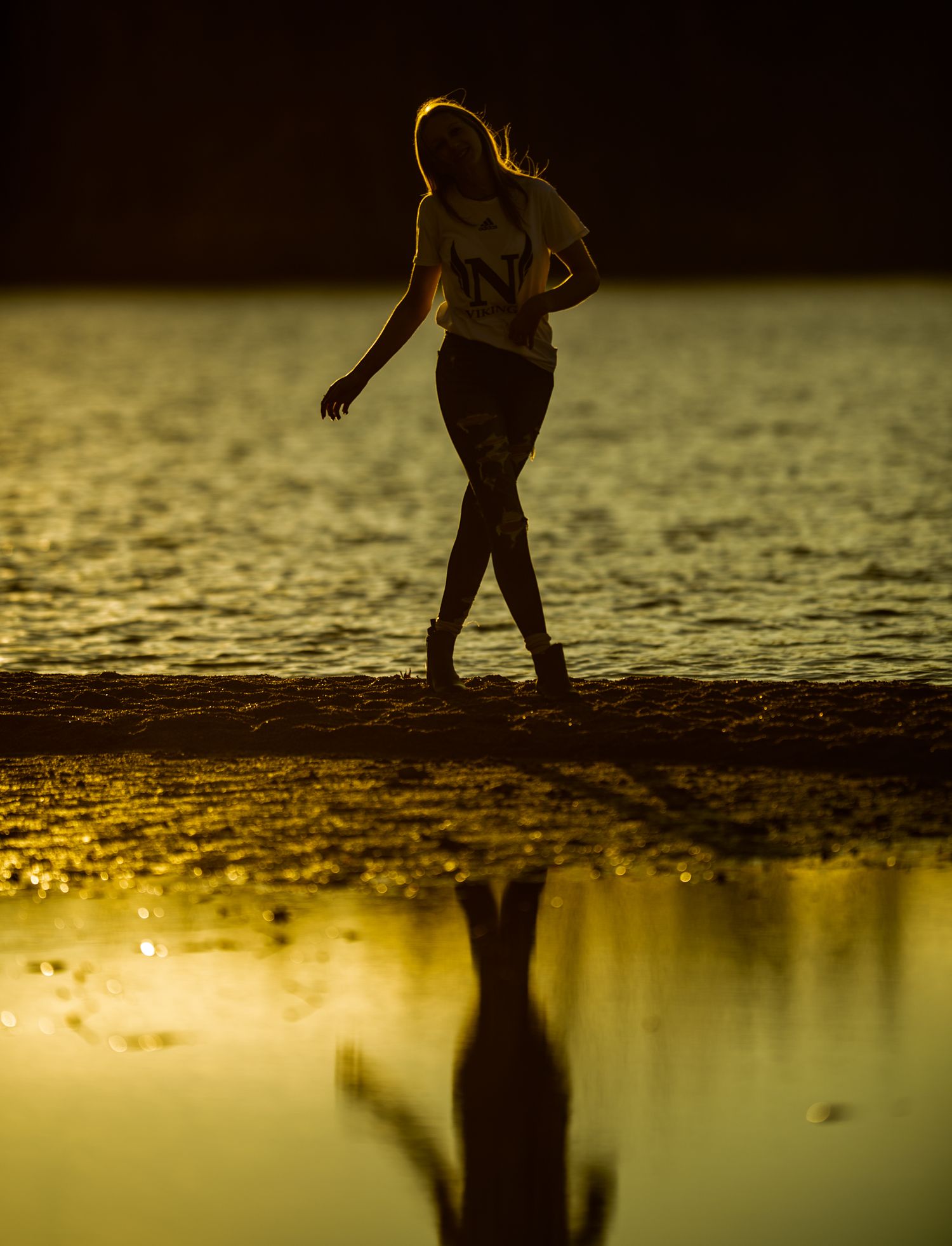 Silhouette of figure walking on beach at sunset with reflection in water.