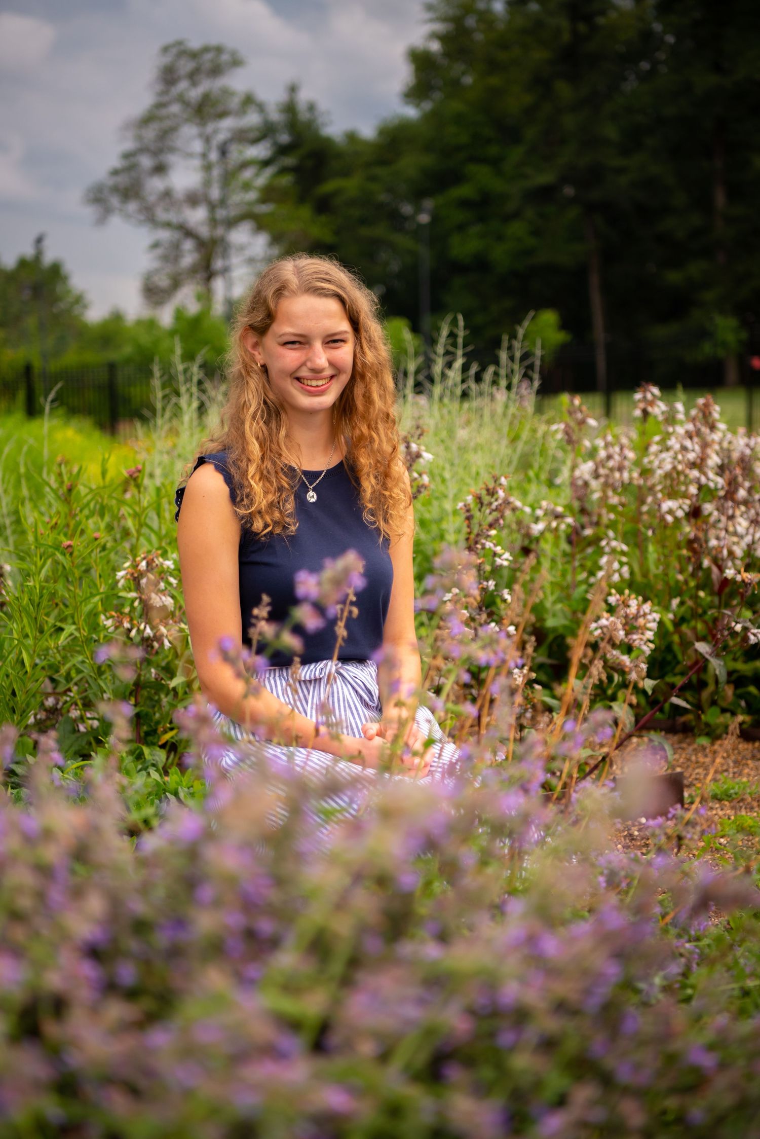 high school senior in a blue shirt sitting in a flower field