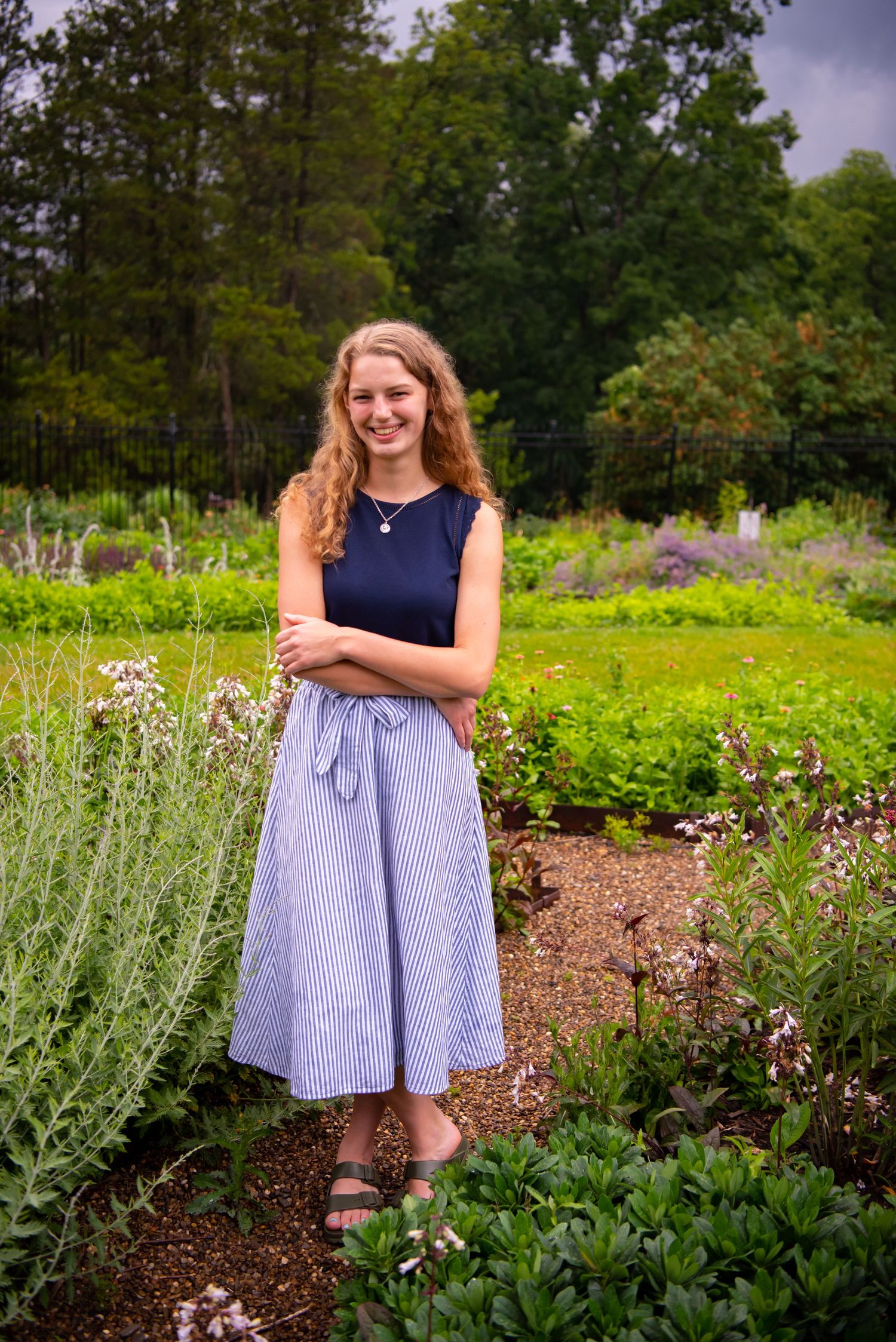 high school senior standing in a flower field in navy shirt and striped skirt
