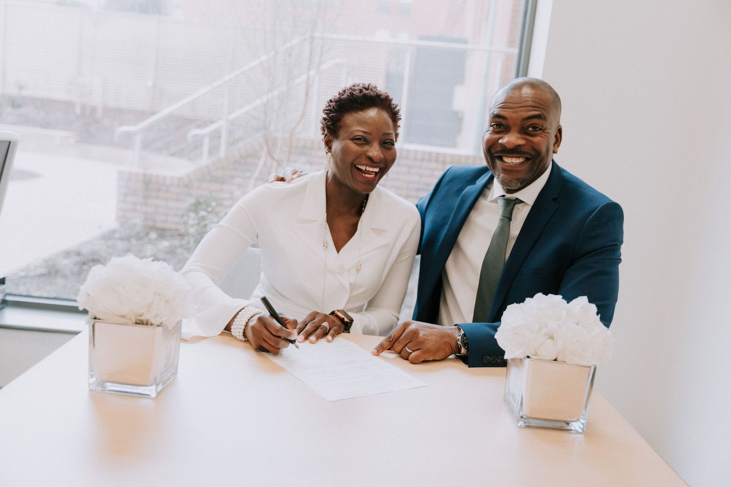 A happy couple shares a joyful moment while signing papers at a conference table.