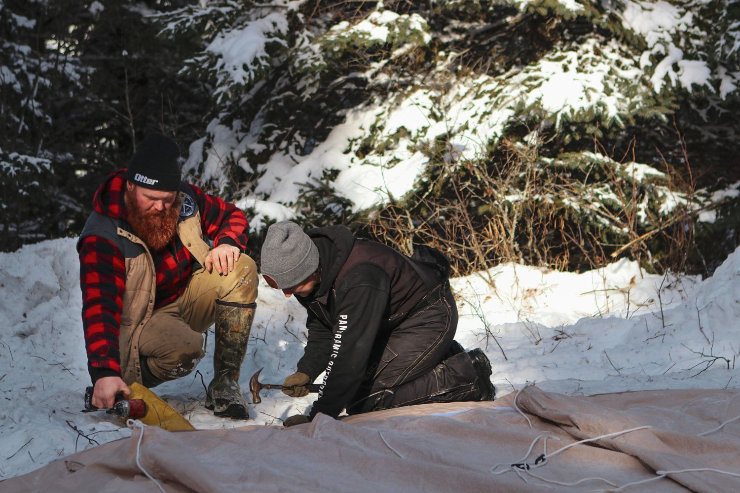 Setting up camping equipment on ground tarp in snowy forest environment.