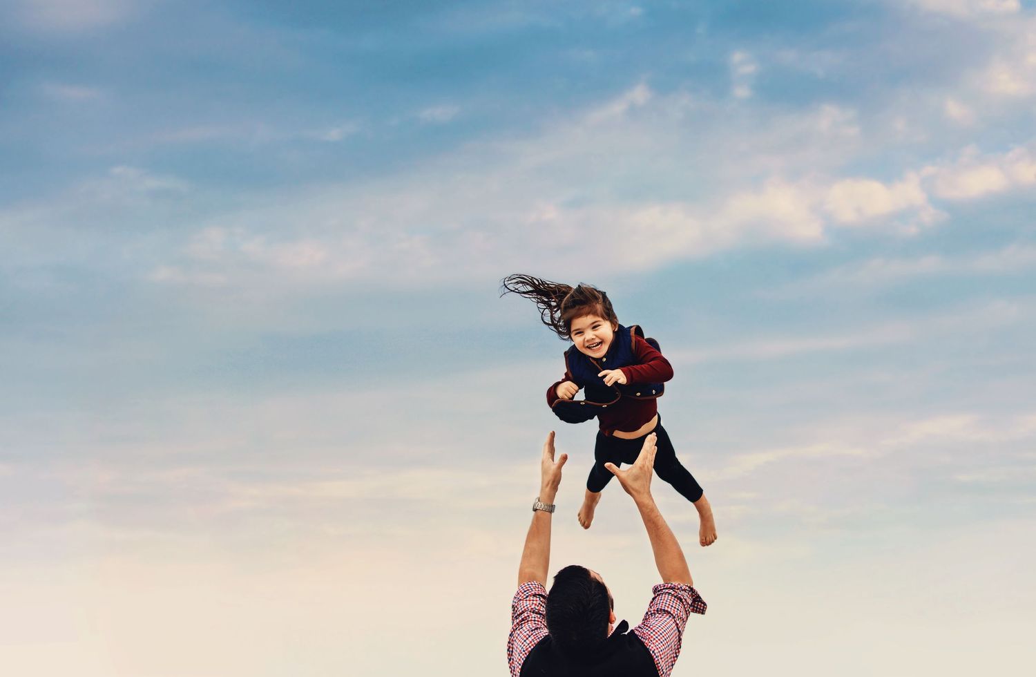 A silhouette of someone lifting a child up against a blue sky backdrop.