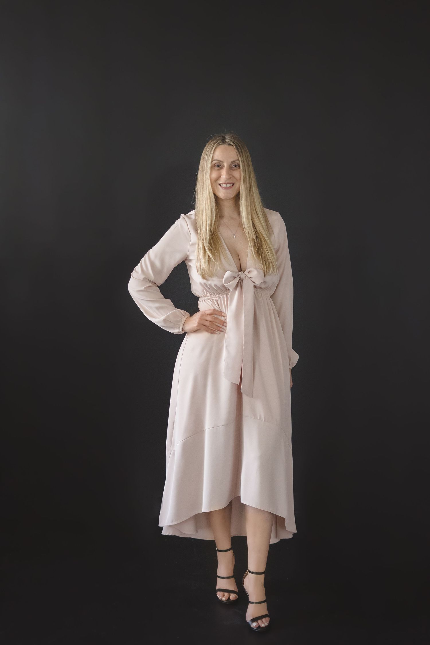 Woman in elegant cream colored dress poses against dark background.