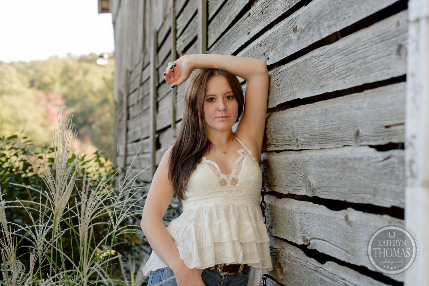 Casual portrait pose leaning against weathered barn wall in summer outfit.