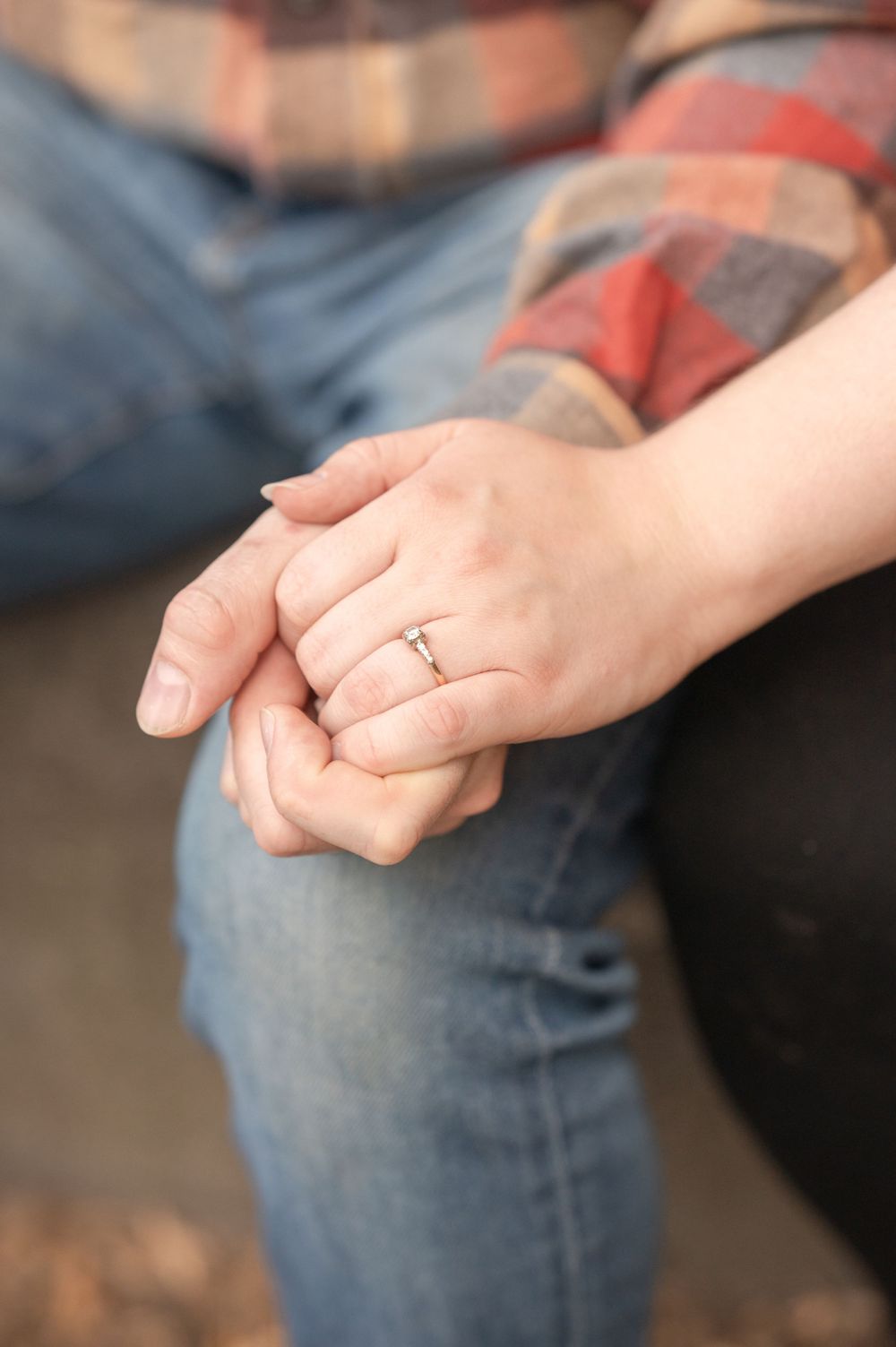 Close-up of clasped hands showing an engagement ring against plaid and denim clothing.