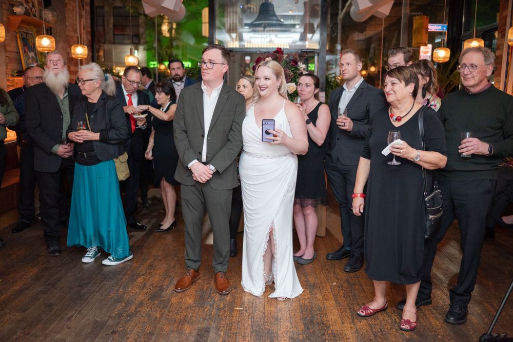 Wedding guests gather in a rustic venue with wooden floors and pendant lighting for a celebration.
