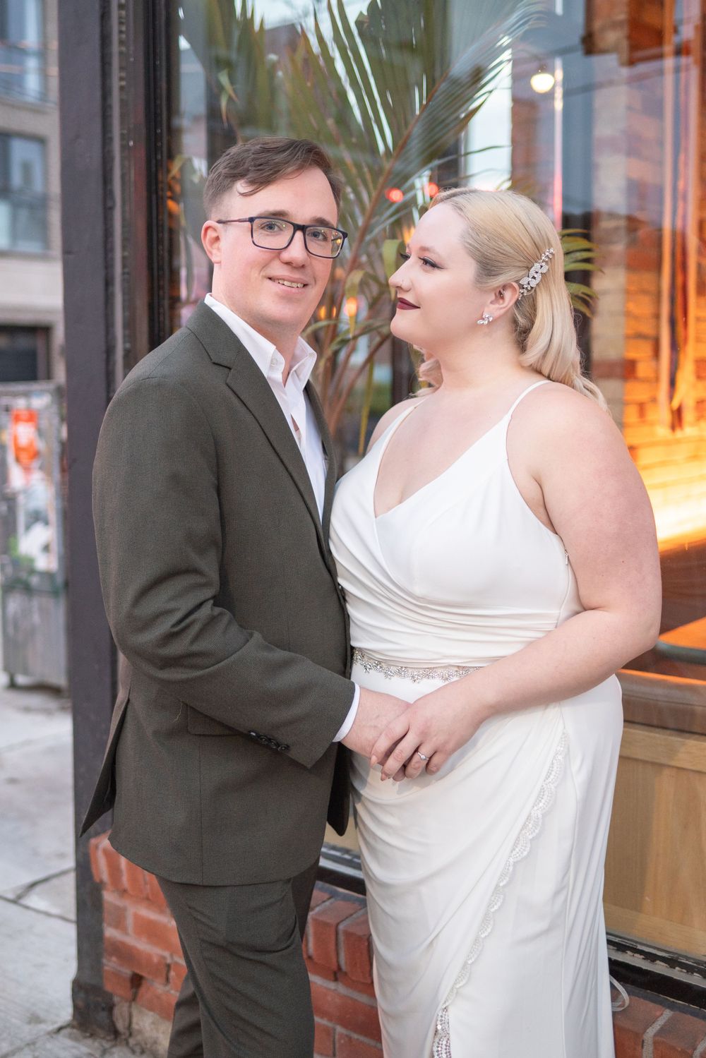 Formal portrait of couple in evening attire against illuminated storefront window.