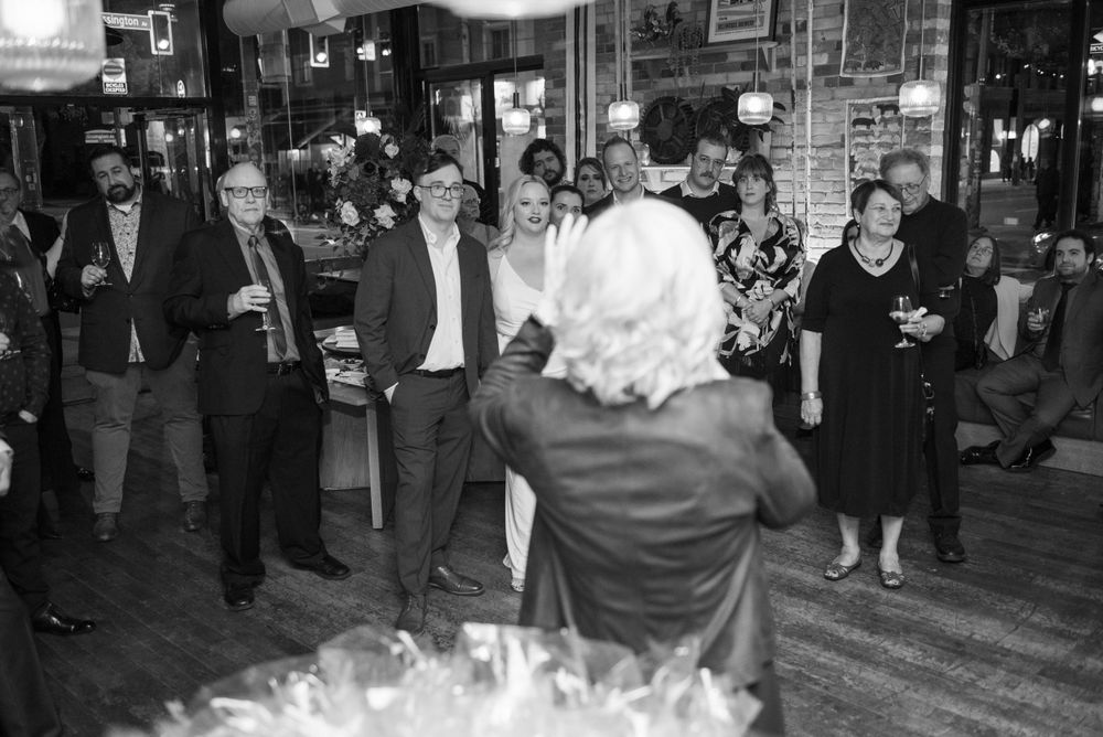 Black and white photo of wedding guests dancing and celebrating in a rustic bar setting.