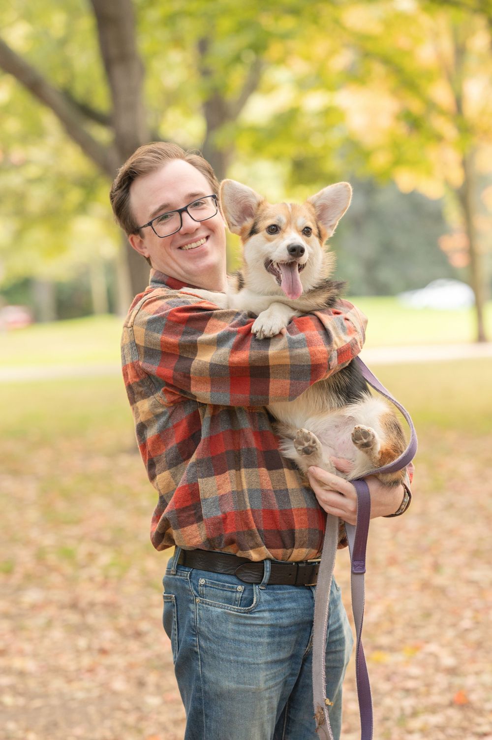 A happy Corgi puppy being held and cuddled outdoors during fall.